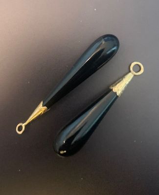 paire de boucles d'oreilles pendantes en verre noir rehaussées de touches dorées sur fond noir