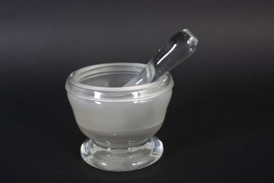 un mortier en verre contenant une cuillère, posé sur une surface noire