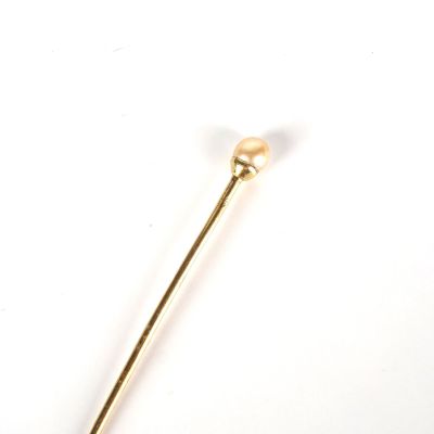 une broche en or ornée d'une perle, posée sur un fond blanc