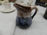 a pitcher sitting on a table with cups and saucers on it