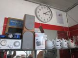 une horloge accrochée au mur au-dessus d'une étagère où sont posées des tasses à café et d'autres objets