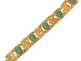 a close up of a gold bracelet with green stones on it