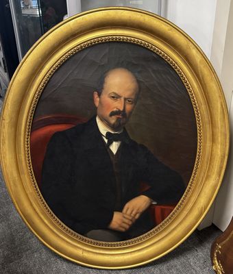 portrait of a man in a black suit and bow tie sitting in a red chair