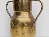 a brass pitcher with a handle on a white surface