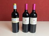three bottles of red wine sitting on a table next to a red wall