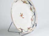 a white plate with a floral design on it on a stand