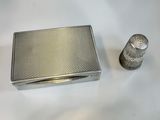 a silver cigarette case and a thimble on a white surface