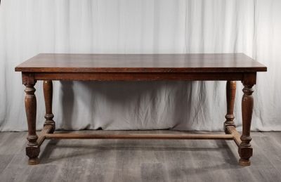 une vieille table en bois posée sur un parquet, à côté d'un rideau blanc