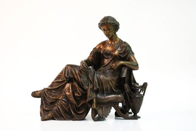 une statue en bronze représentant une femme assise sur une chaise