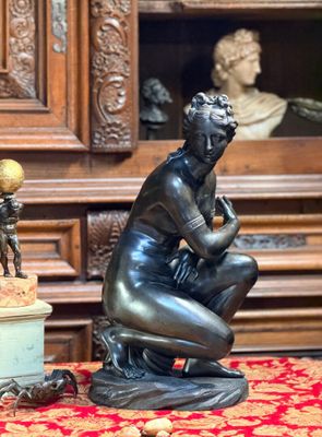 une statue représentant une femme assise sur une table, à côté d'un vase