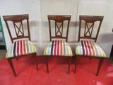 three wooden chairs with colorful striped upholstered seats on a red carpet