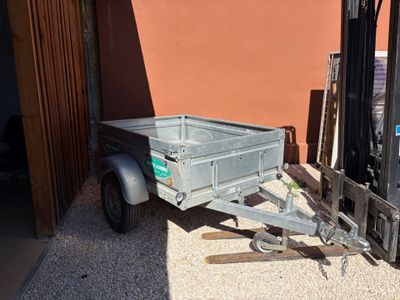 un chariot élévateur auquel est attelée une remorque, devant un bâtiment