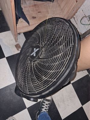 une personne debout à côté d'un ventilateur, sur un sol à damier