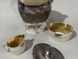 a silver tea pot and two silver cups on a white table