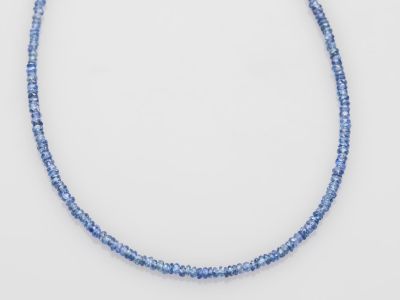 un gros plan d'un collier de perles bleues posé sur une surface blanche