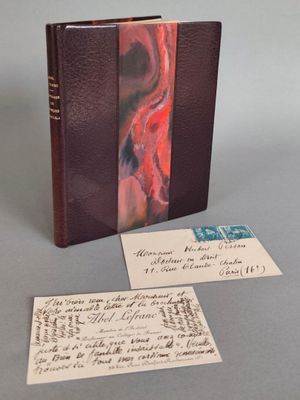 un livre à la couverture rouge posé sur une table, à côté d'une feuille de papier