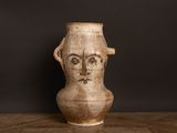 un vase marron orné d'un visage, posé sur une table