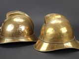 pair of antique brass fire helmets on a black background