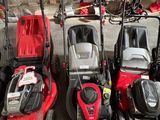 Plusieurs tondeuses à gazon sont alignées dans un garage
