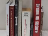 Plusieurs livres sont alignés sur une table blanche, avec une horloge en arrière-plan.