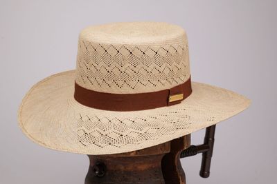 chapeau de paille beige orné d'un ruban en cuir marron, posé sur un support en bois
