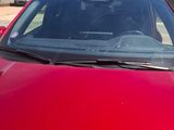 the front of a red car parked in a lot next to a building