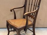 Une vieille chaise en bois avec une assise tressée est posée devant un mur.