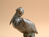 statue of a pelican sitting on a tree stump on a beige background