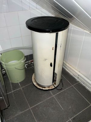 a water heater in the corner of a bathroom next to a trash can