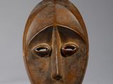 une paire de masques en bois sculptés posés sur un socle, sur fond blanc