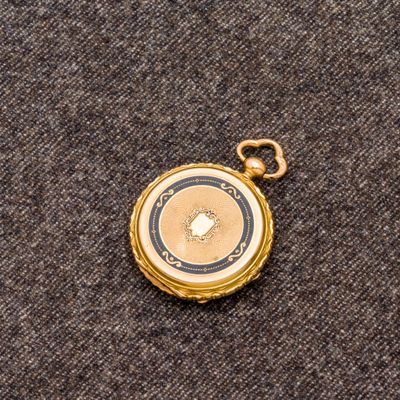 une image représentant une montre de poche en or posée sur un tissu gris