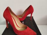 des chaussures à talons hauts rouges posées sur une boîte noire, elle-même posée sur une surface blanche