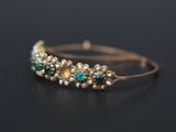 a close up of a gold bracelet with green stones and pearls