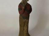 une vieille statue en bois représentant une femme portant un chapeau et une chemise rouge