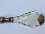 une cuillère en argent avec un manche en verre posée sur une surface blanche