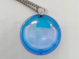 un pendentif en verre bleu muni d'une chaîne en argent, posé sur une surface blanche