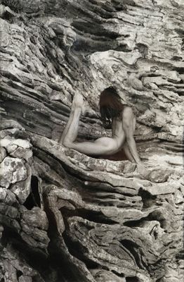 a nude woman sitting on a rock with her legs crossed