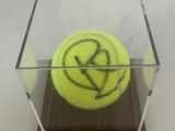 une balle de tennis jaune dans une boîte transparente posée sur une table