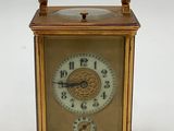 une petite horloge dorée munie d'une poignée, sur fond blanc