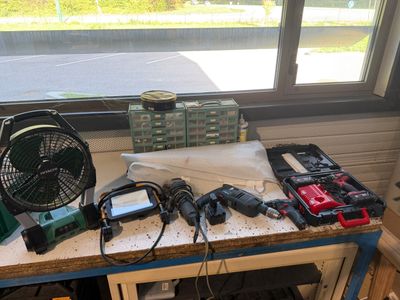 une table sur laquelle se trouvent des outils, avec un ventilateur posé dessus