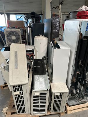 Plusieurs climatiseurs sont empilés sur des palettes dans un garage