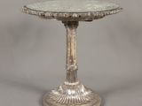 une table plaquée argent avec un plateau en verre sur fond gris