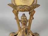 une horloge en or posée sur un socle, sur laquelle est assise une femme