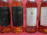 four bottles of wine are lined up on a pink background