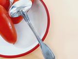 three tomatoes on a plate with a spoon in it