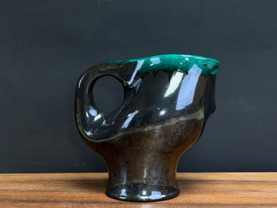 black and green vase on wooden table against black wall