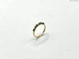 un gros plan d'une bague en or sertie de pierres vertes sur un fond blanc