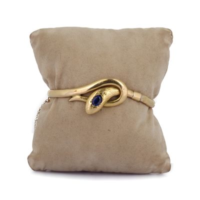 une photo d'un bracelet en or orné d'une pierre bleue, posé sur un coussin