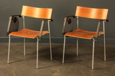 two wooden chairs sitting next to each other in front of a gray wall