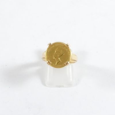 bague en or jaune surmontée d'une pièce, posée sur un fond blanc
